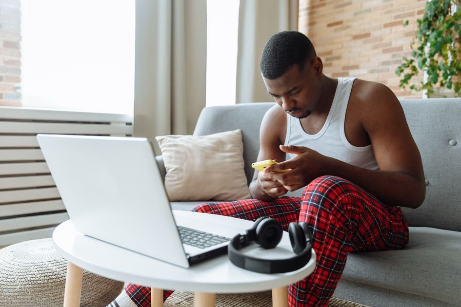 A man multitasking with a laptop and smartphone in a living room