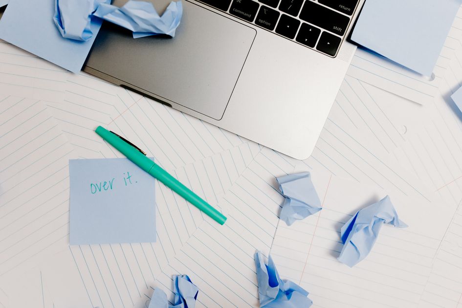 A messy desk with a laptop and a post-it note among crumpled papers