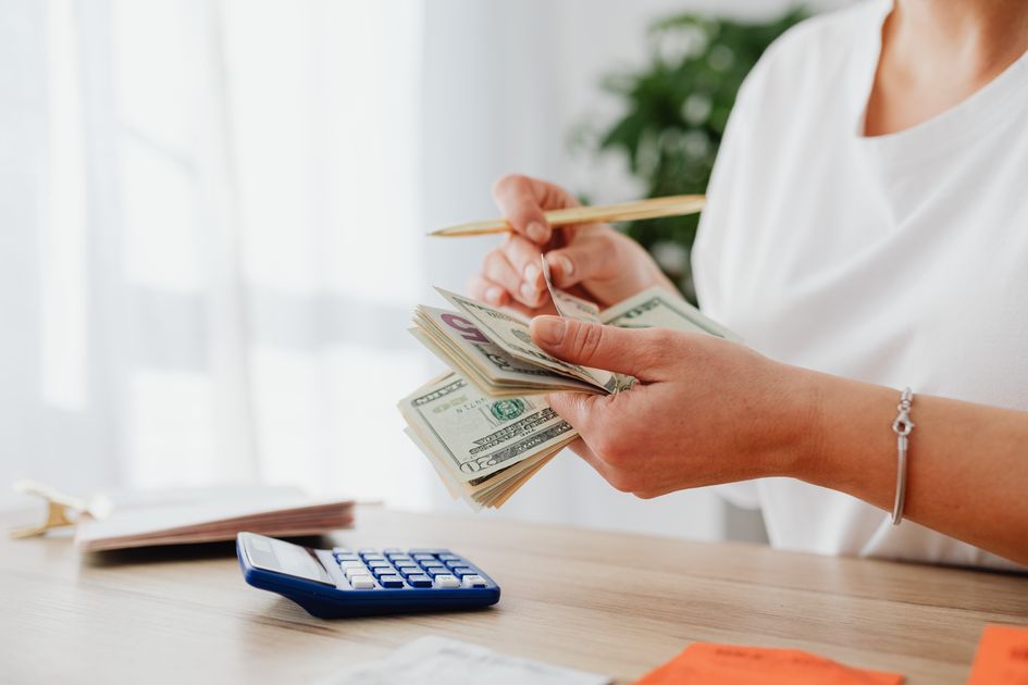 A woman holding US dollars, calculating finances at home