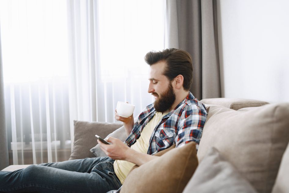 A man enjoying coffee on a sofa while browsing his phone