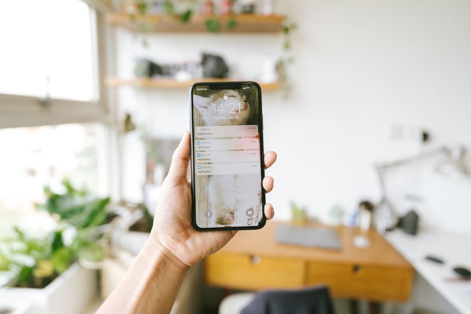 A hand holding a smartphone in a blurred office setting