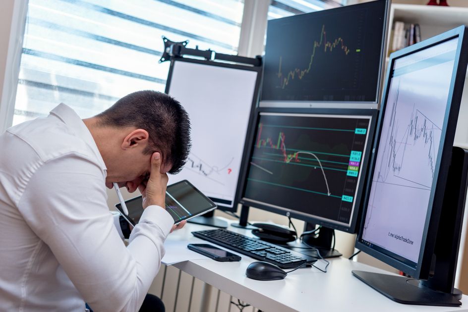 A stressed trader analyzing market data on multiple monitors