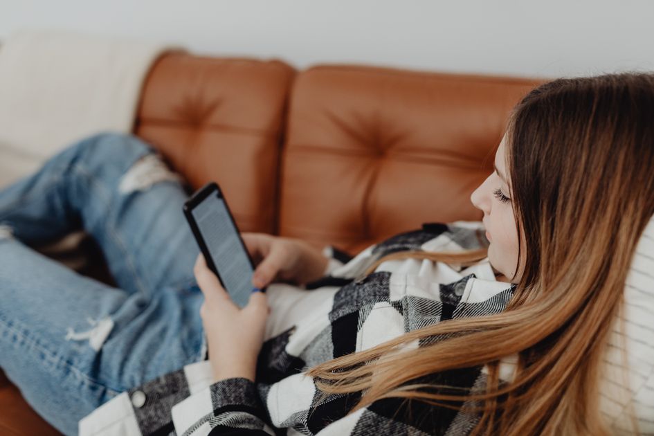 A woman lying on a sofa checking her smartphone