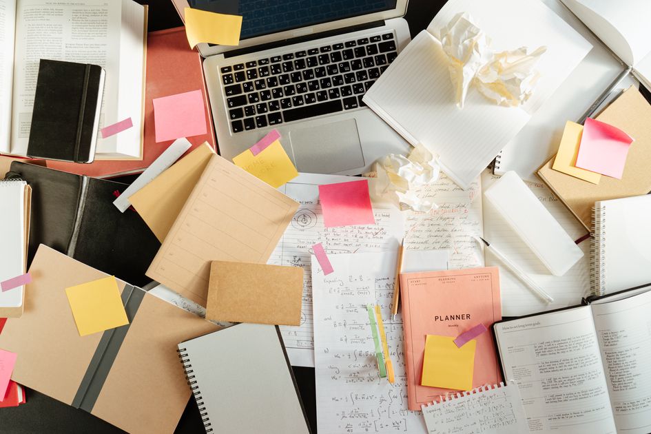 A messy study desk with a laptop, notebooks, and sticky notes