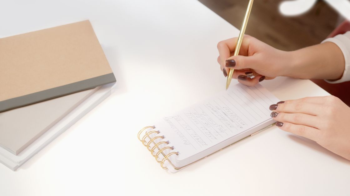 Hands writing in a spiral notebook on a desk