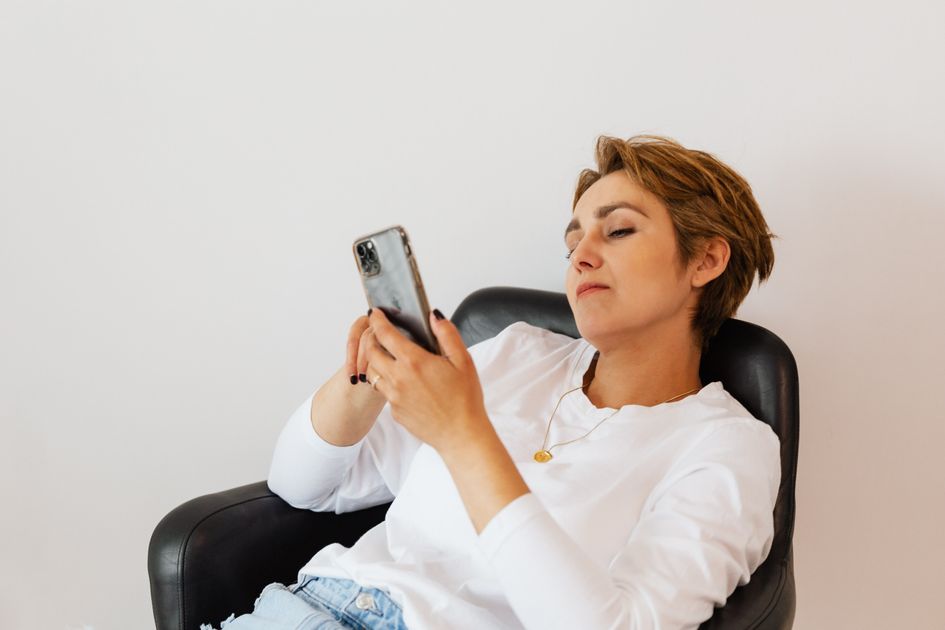 A woman browsing social media on her phone in a leather armchair