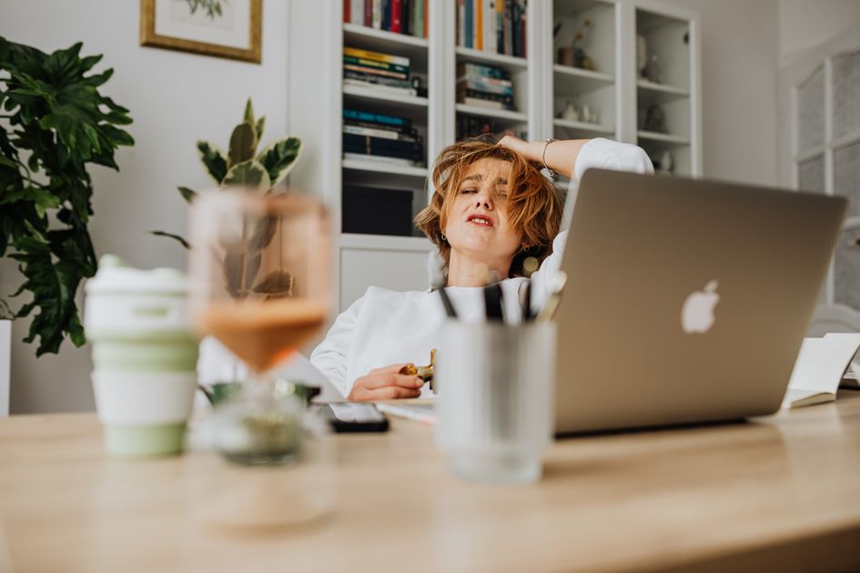 A woman feeling stressed while working from home at a desk with a laptop