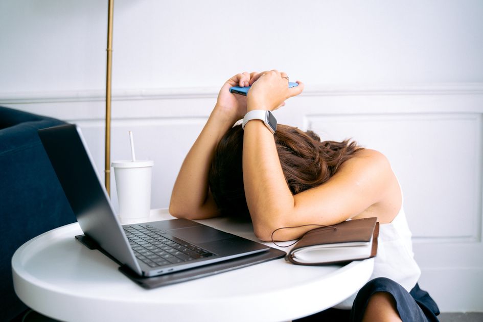 A young woman showing stress with a laptop and phone at her desk