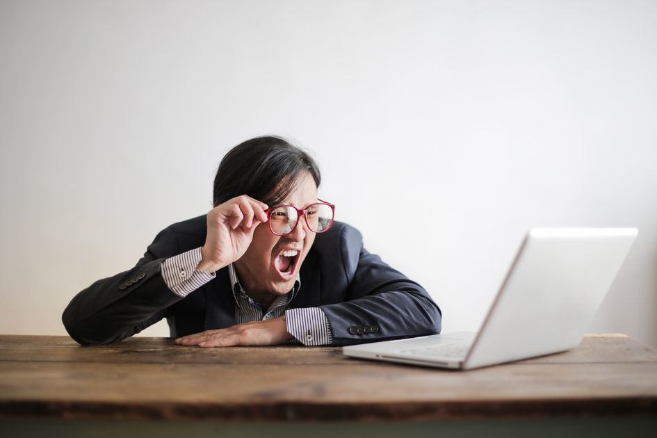 A man in glasses looking at a laptop with mouth wide open