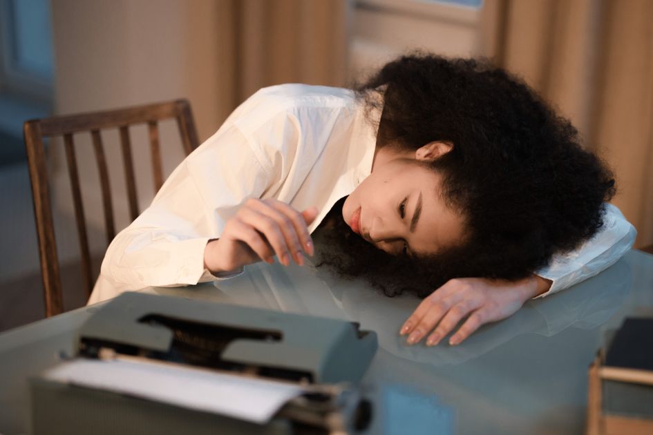 A woman with afro hair resting on a table beside a vintage typewriter