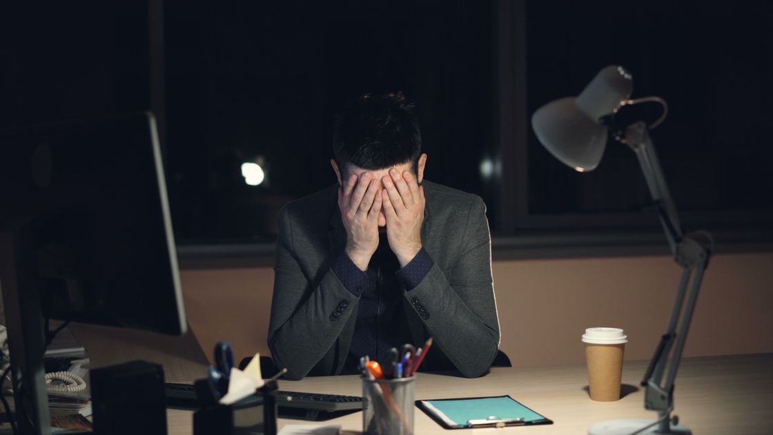 A tired man in an office environment, working late by lamplight