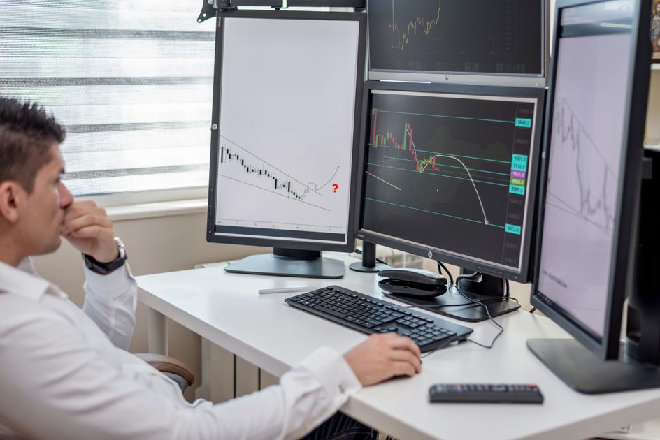A professional analyzing financial data on multiple computer monitors