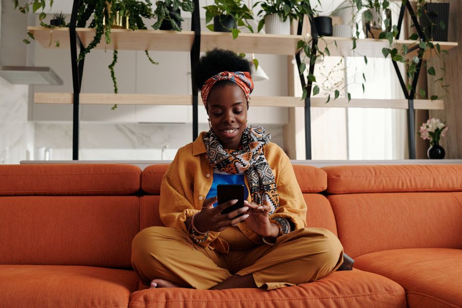A woman sitting on a sofa smiling while using a smartphone