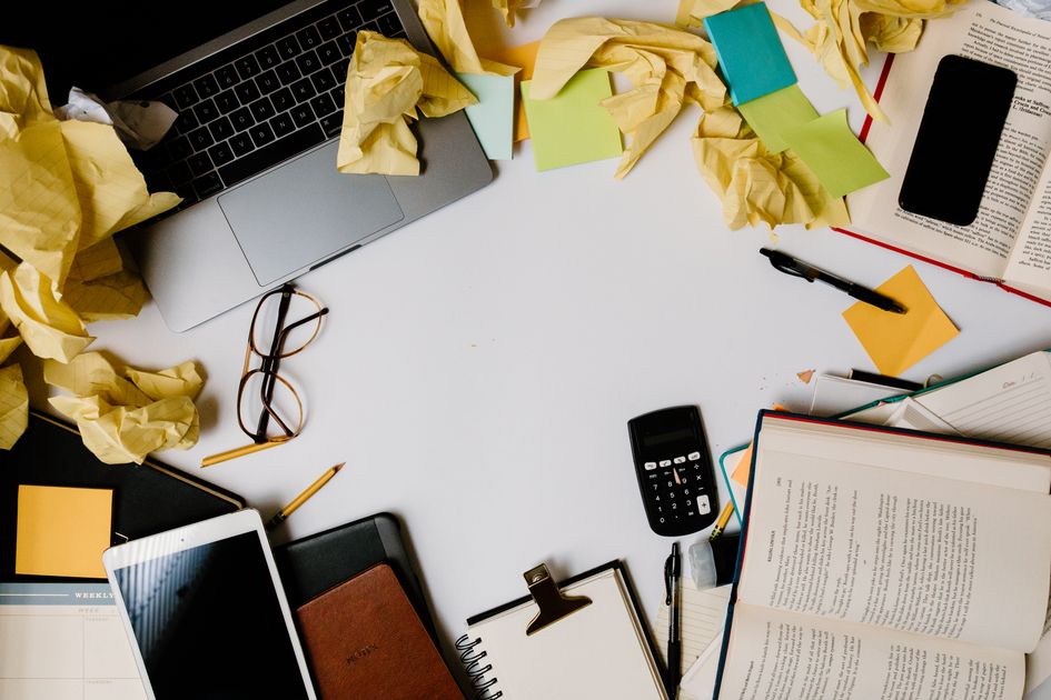 A messy desk with electronics and scattered notes