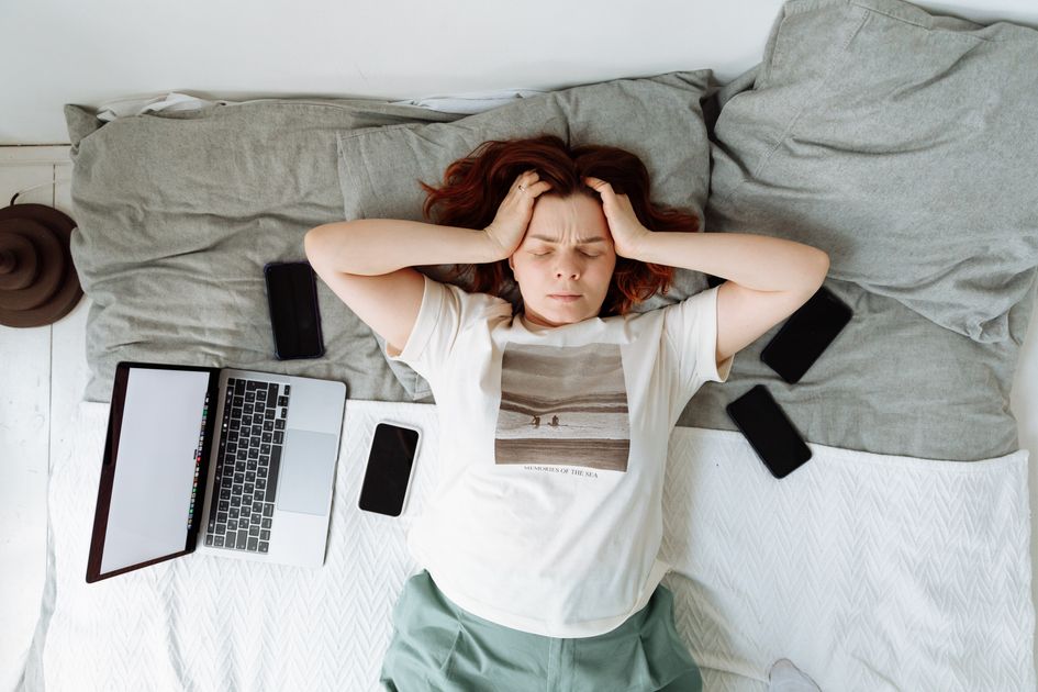 A distressed woman lying in bed surrounded by digital devices
