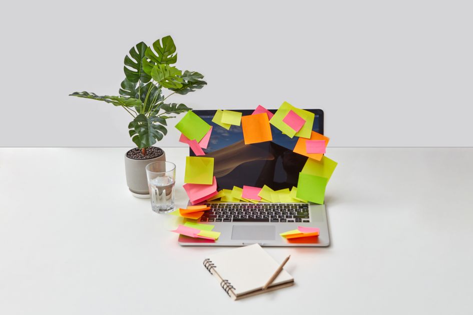 A laptop covered with colorful sticky notes on a desk