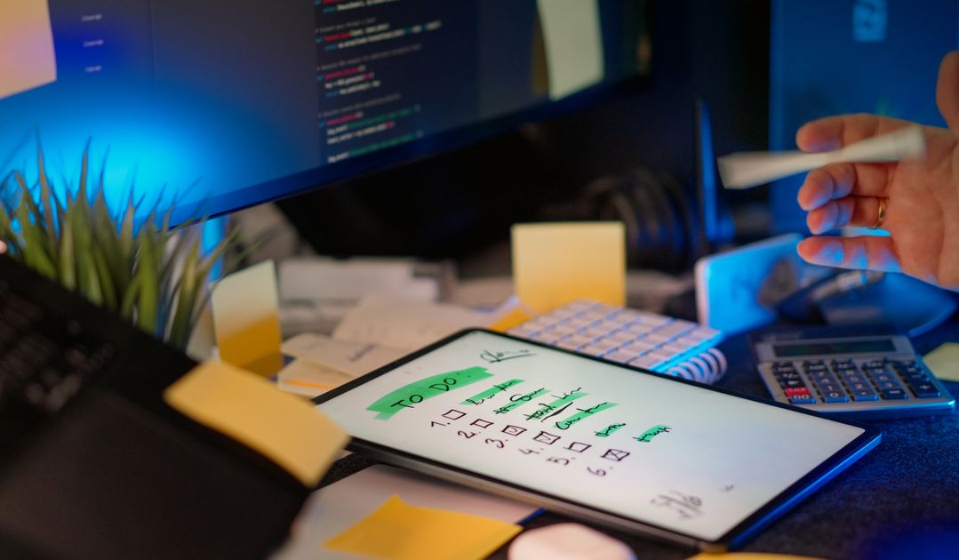 A cluttered desk with a to-do list and office supplies
