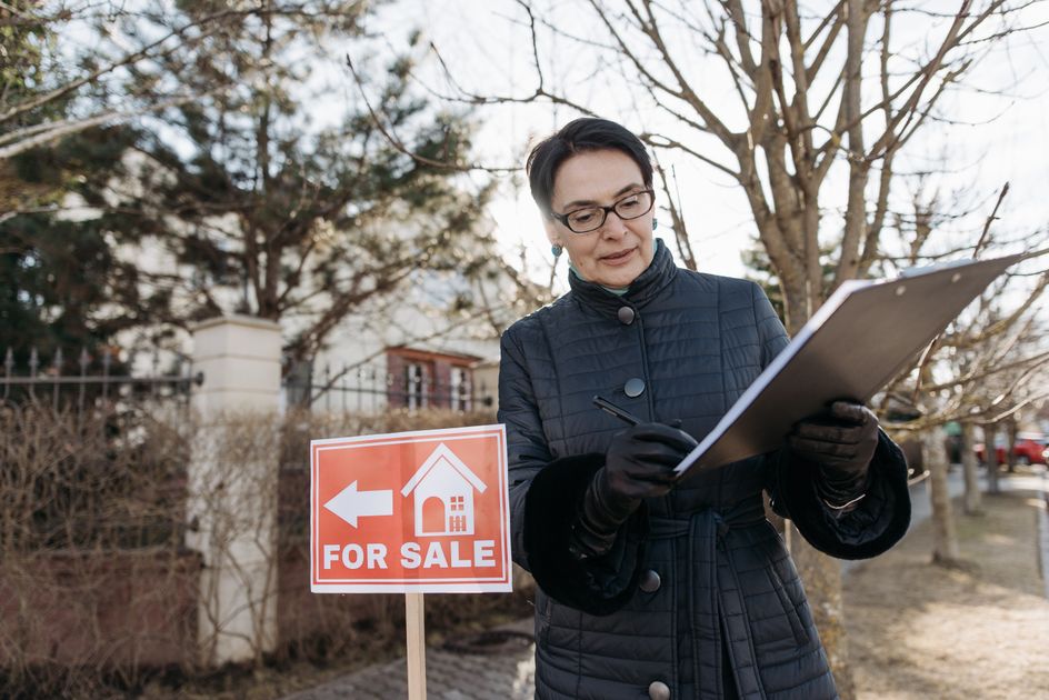 A real estate agent reviewing a clipboard beside a sign