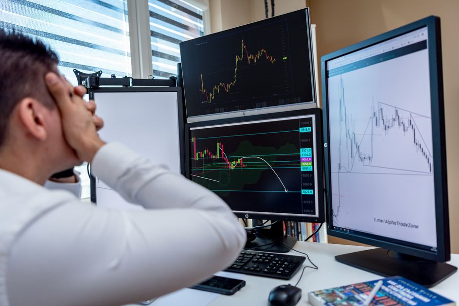 A businessman holds his head in frustration at a desk with financial charts