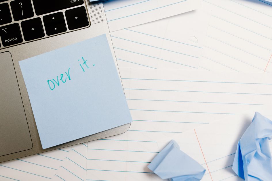 A laptop with a sticky note beside a notebook and papers