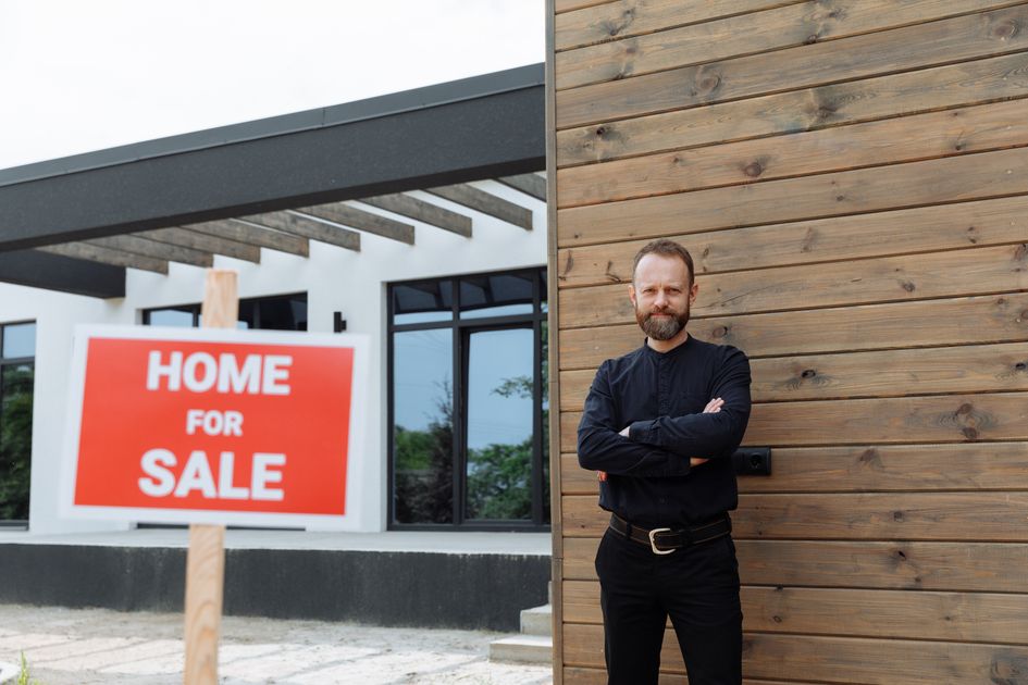 A real estate agent standing by a modern home for-sale sign