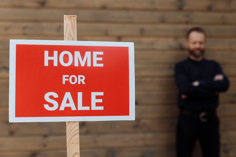 A real estate agent standing beside a for-sale sign on a wooden wall