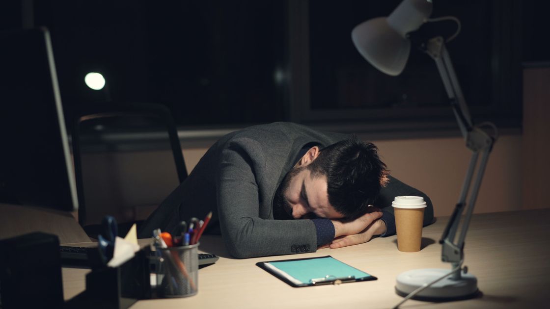 A person asleep at their desk beside a coffee cup