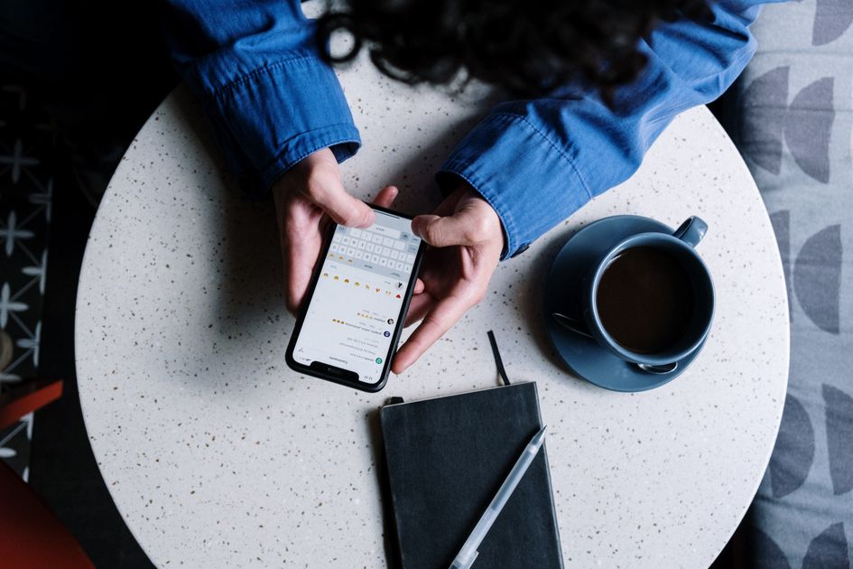A person using a smartphone at a table with a notebook and coffee