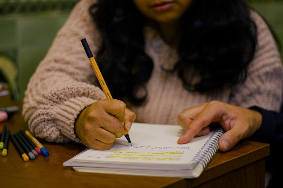 A person writing in a journal with colored pens on a desk